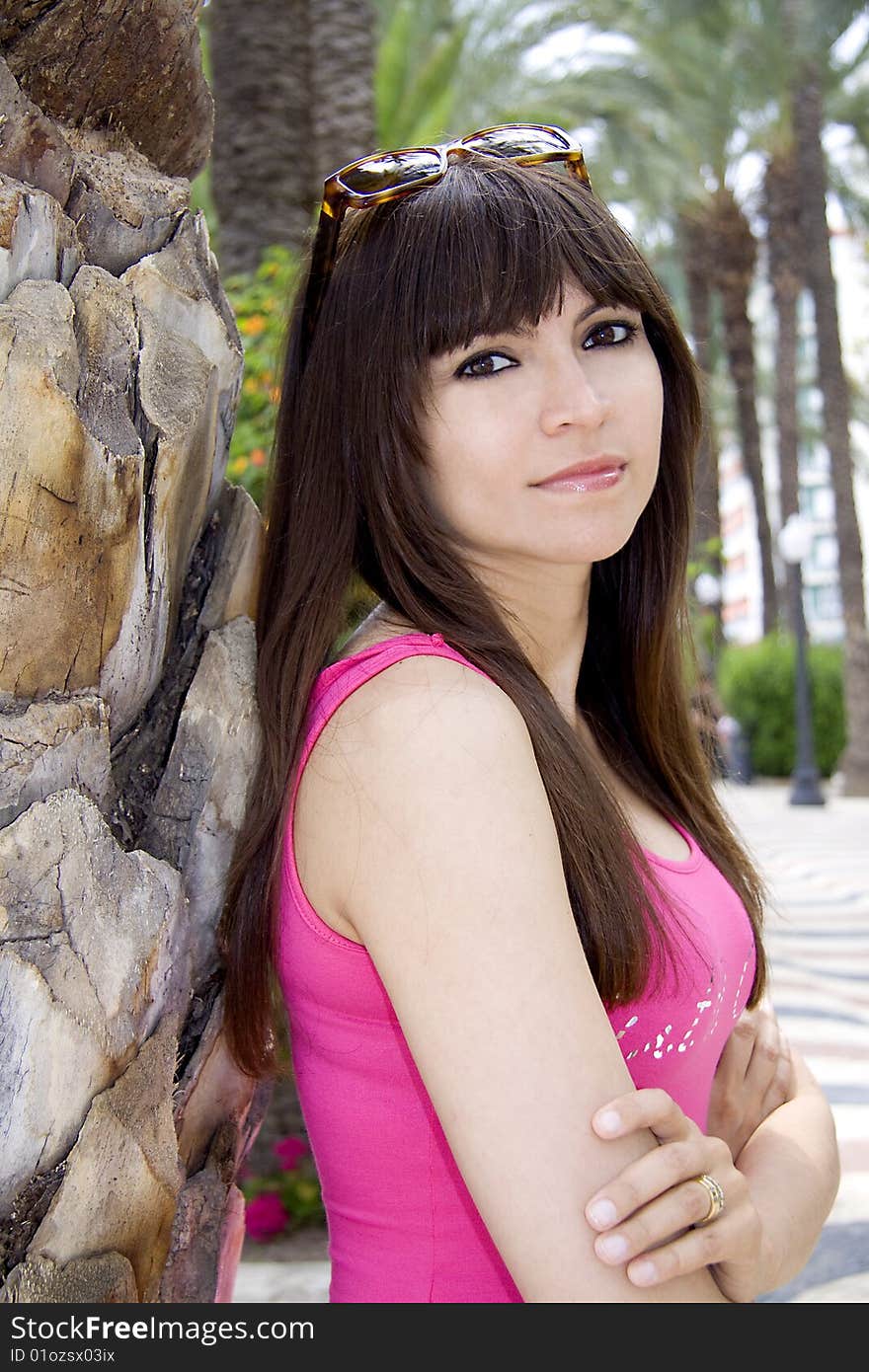 Beautiful woman with a pink top leaning op against a palm tree. Beautiful woman with a pink top leaning op against a palm tree