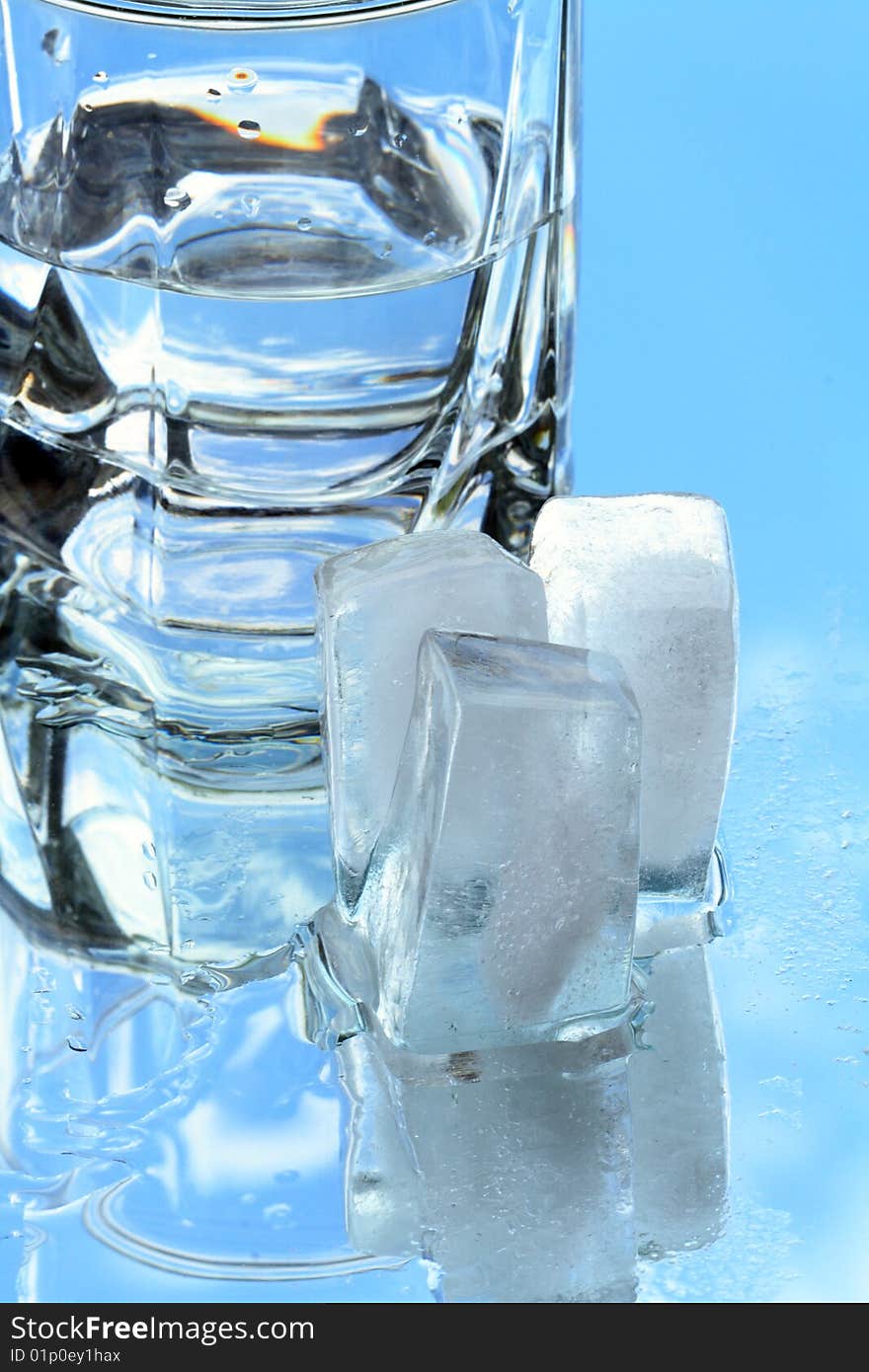 Ice cubes lying near glass of water on background with blue sky. Ice cubes lying near glass of water on background with blue sky