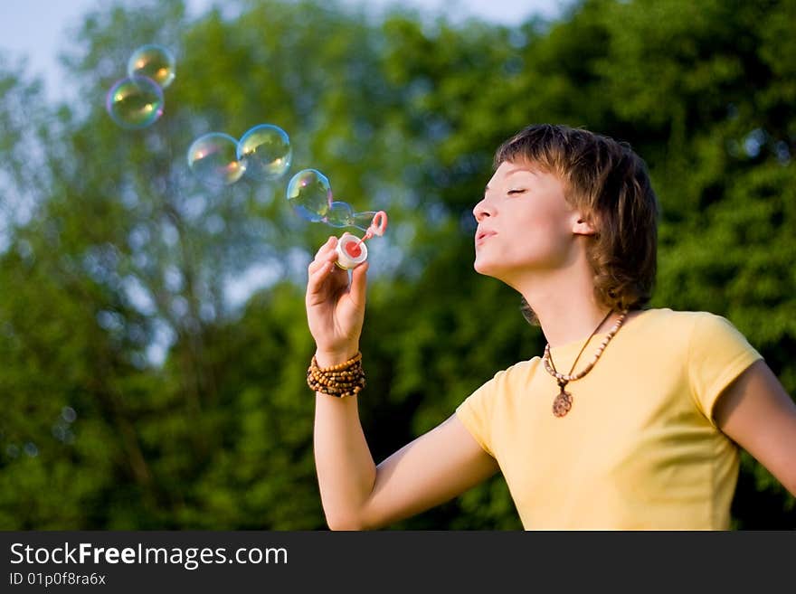 A young woman blowing up soap-bubbles on the green trees background. A young woman blowing up soap-bubbles on the green trees background