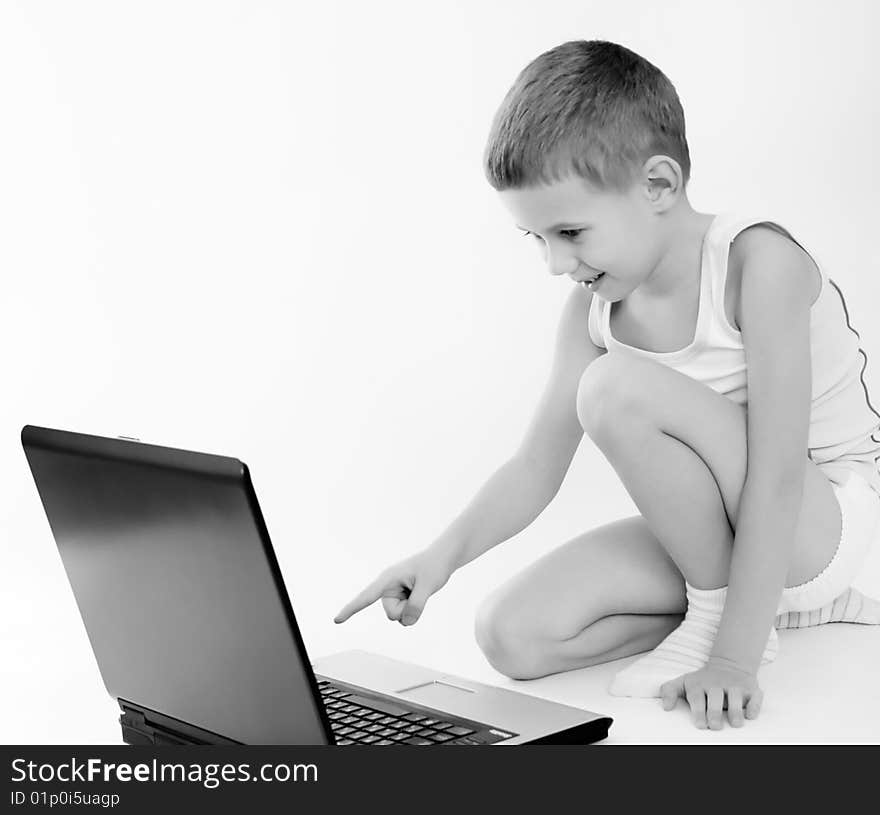 The little boy in a vest sits on a floor and looks on laptop. The little boy in a vest sits on a floor and looks on laptop