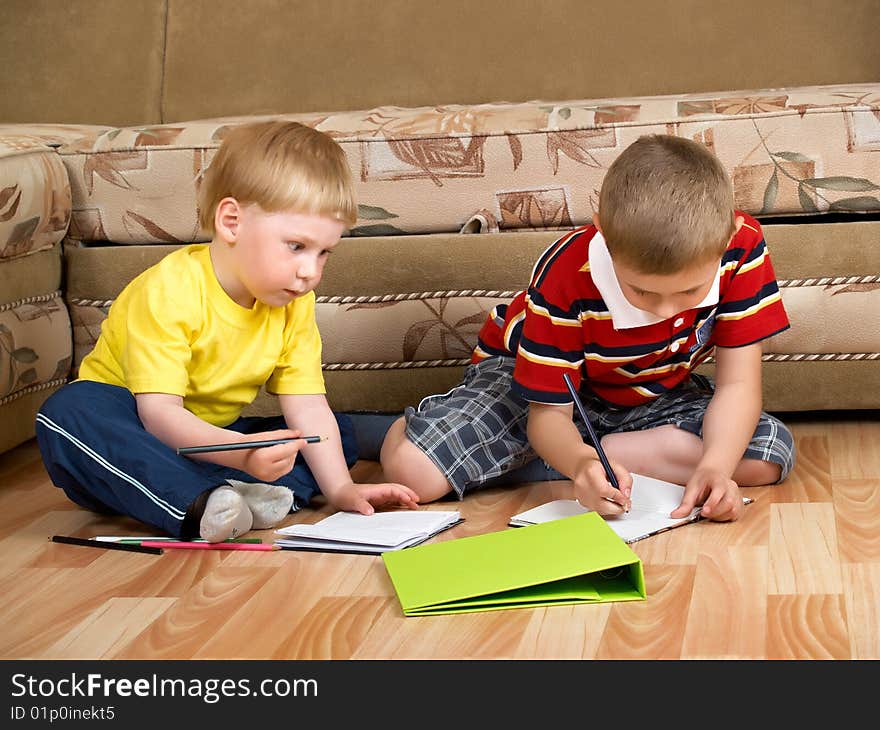 Two boys draw with paints sitting on floor