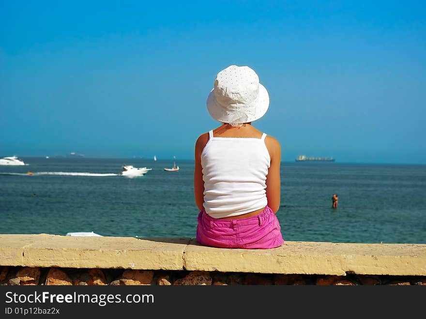 Girl is sitting on a border of the beach and looking at the horizon. Girl is sitting on a border of the beach and looking at the horizon