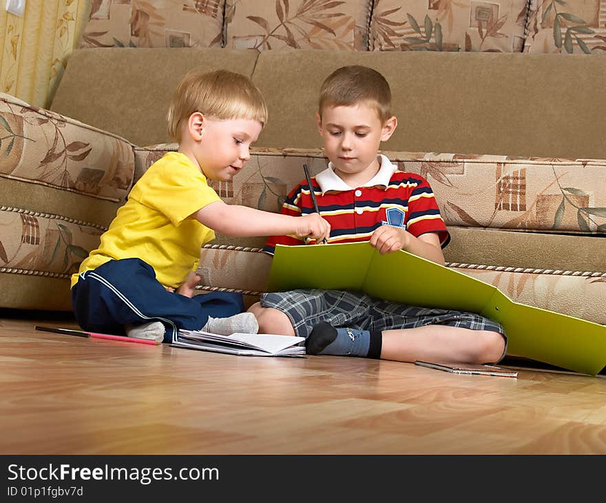 Two boys draw with paints sitting on floor