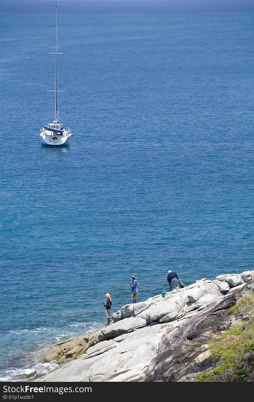 Beautiful yacht in the ocean and fishermen on the rocks. copy space. Beautiful yacht in the ocean and fishermen on the rocks. copy space