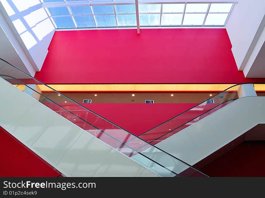 Pair of rolling stairs with red wall in background and glass roof above