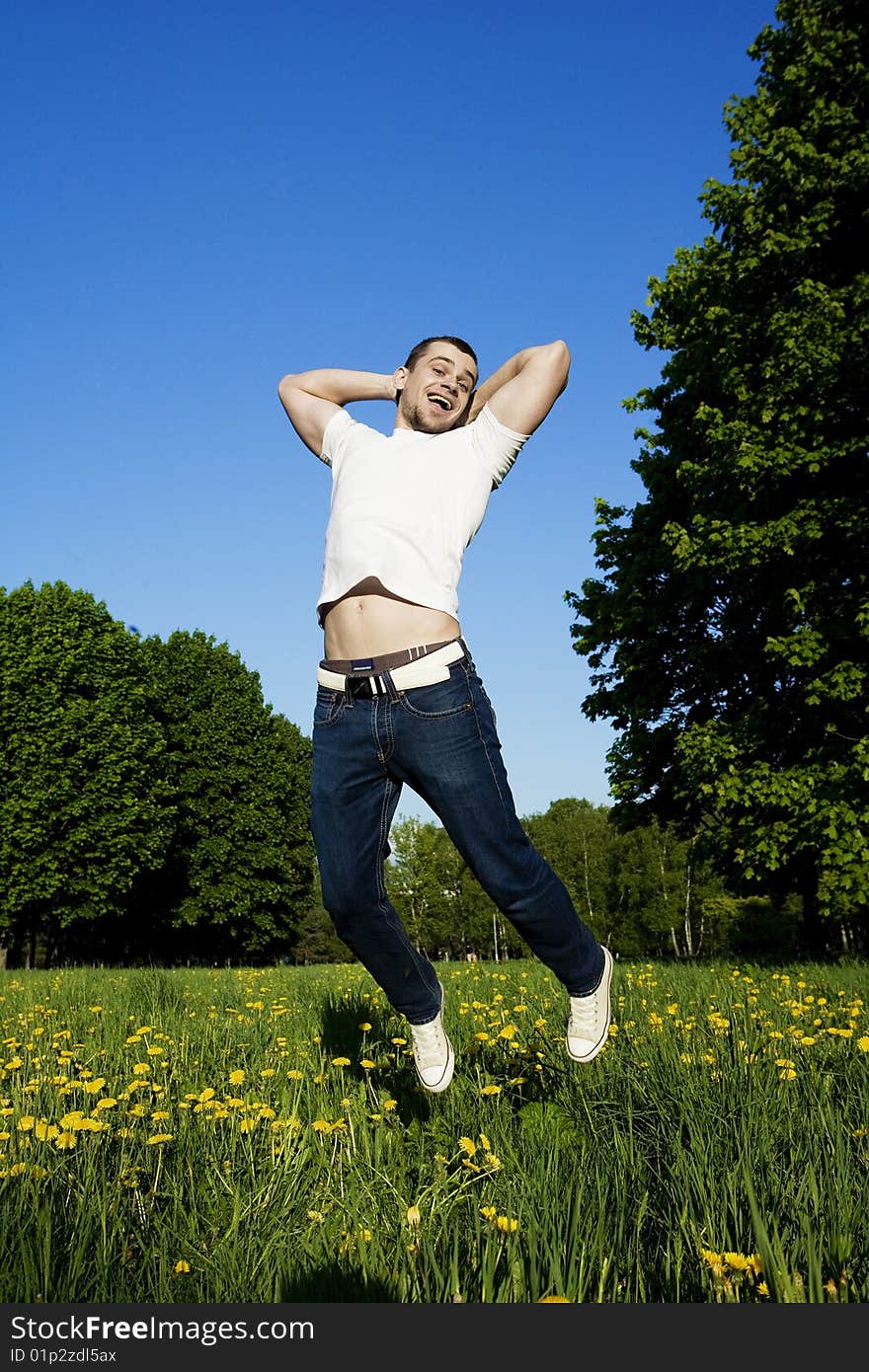 The beautiful young man in park jumps in the sky. Laughs, hands behind a head. In a vest white, jeans and gym shoes. The beautiful young man in park jumps in the sky. Laughs, hands behind a head. In a vest white, jeans and gym shoes