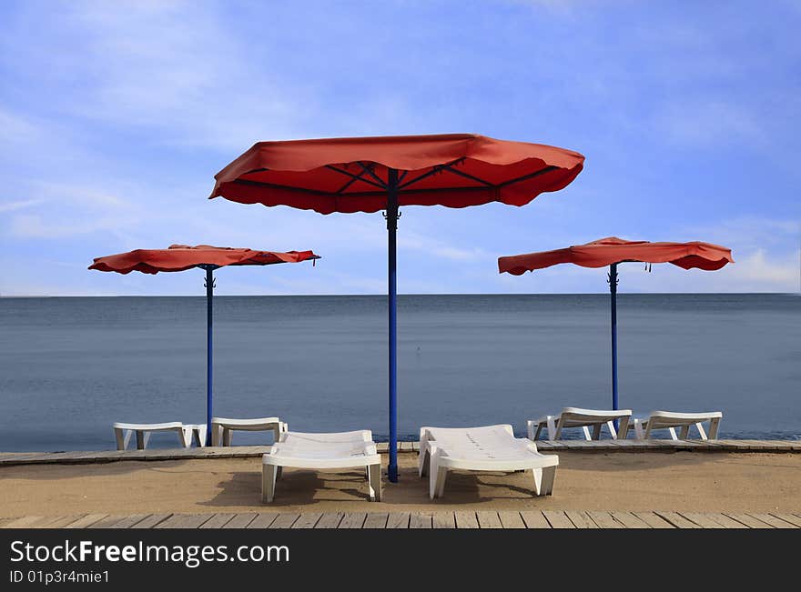 Image of red parasols and white sunbeds on a beach. Image of red parasols and white sunbeds on a beach