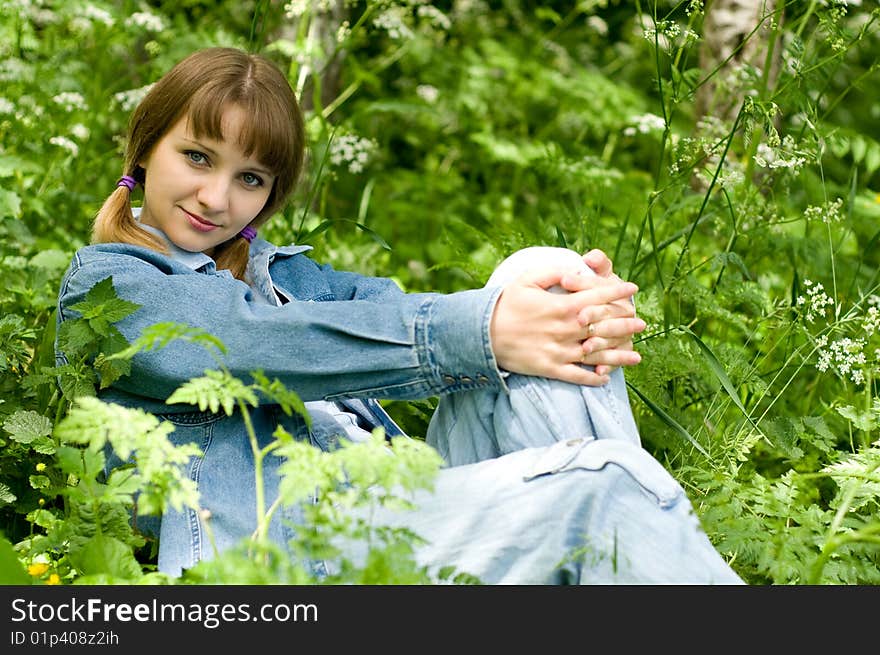 The beautiful girl in park sits on a green grass