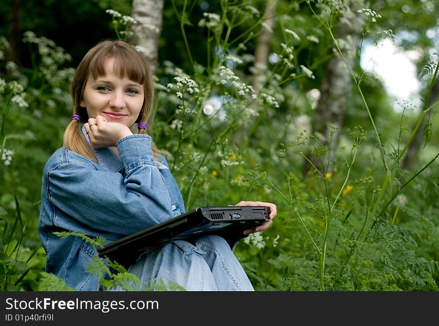 The beautiful girl with the laptop in park sits in a green grass. The beautiful girl with the laptop in park sits in a green grass