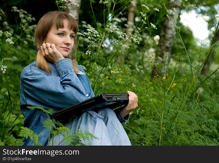 The beautiful girl with the laptop in park sits in a green grass. The beautiful girl with the laptop in park sits in a green grass