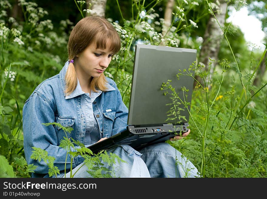 The beautiful girl with the laptop in park sits in a green grass. The beautiful girl with the laptop in park sits in a green grass