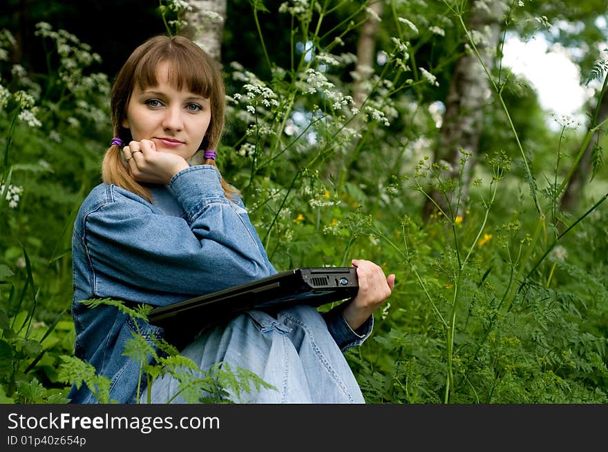 The beautiful girl with the laptop in park sits in a green grass. The beautiful girl with the laptop in park sits in a green grass