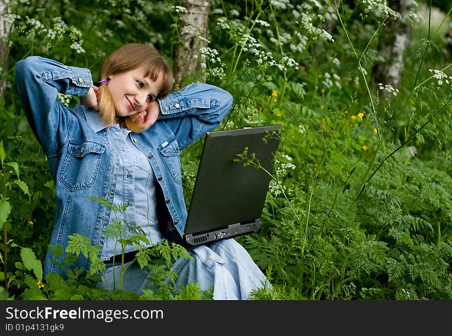 The beautiful girl with the laptop in park sits in a green grass. The beautiful girl with the laptop in park sits in a green grass