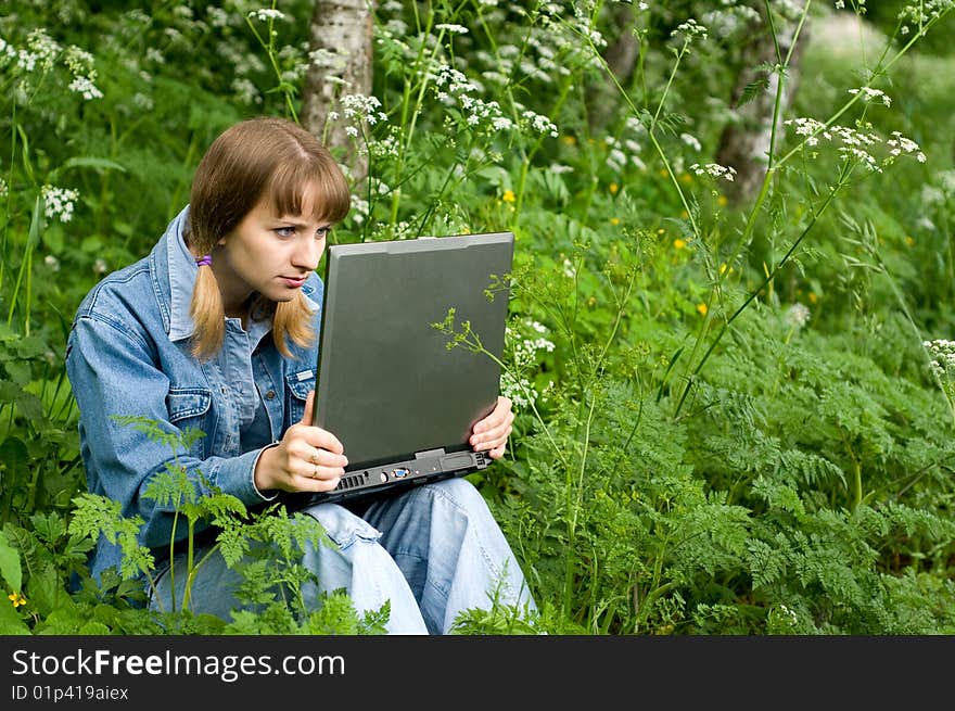 The beautiful girl with the laptop in park sits in a green grass. The beautiful girl with the laptop in park sits in a green grass