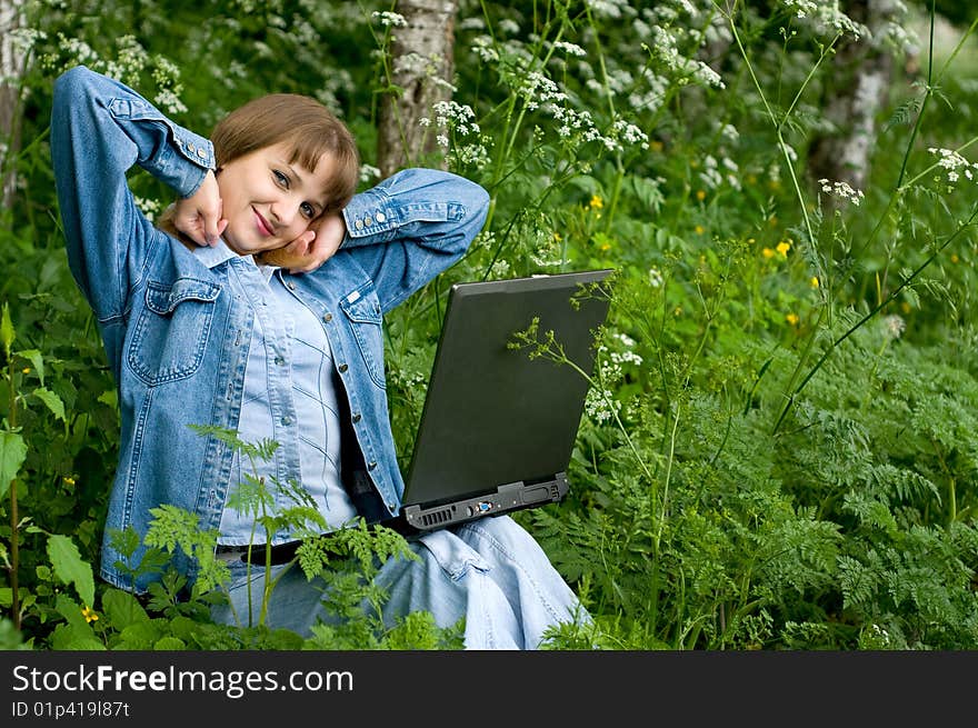 The beautiful girl with the laptop in park sits in a green grass. The beautiful girl with the laptop in park sits in a green grass