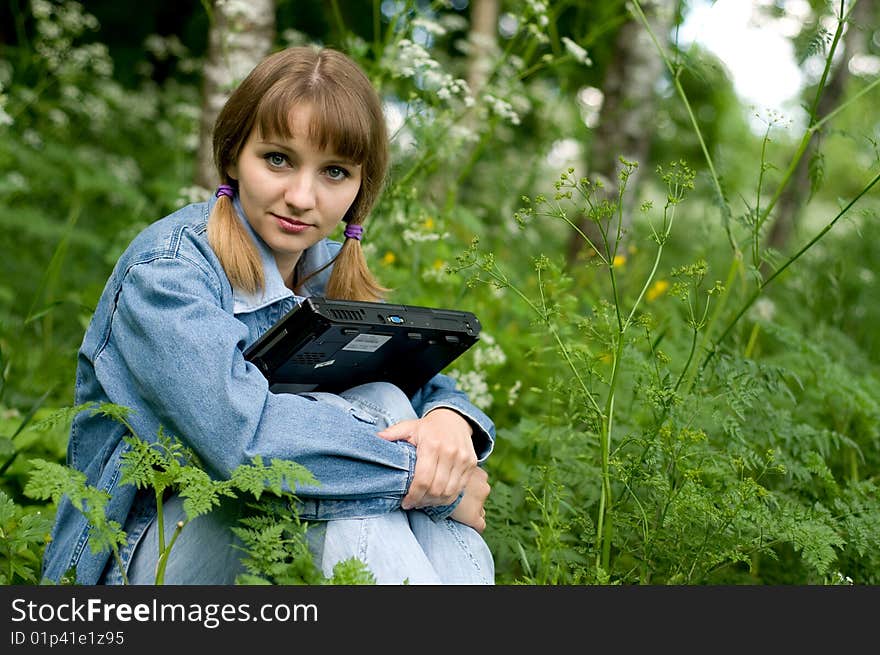 The beautiful girl with the laptop in park sits in a green grass. The beautiful girl with the laptop in park sits in a green grass