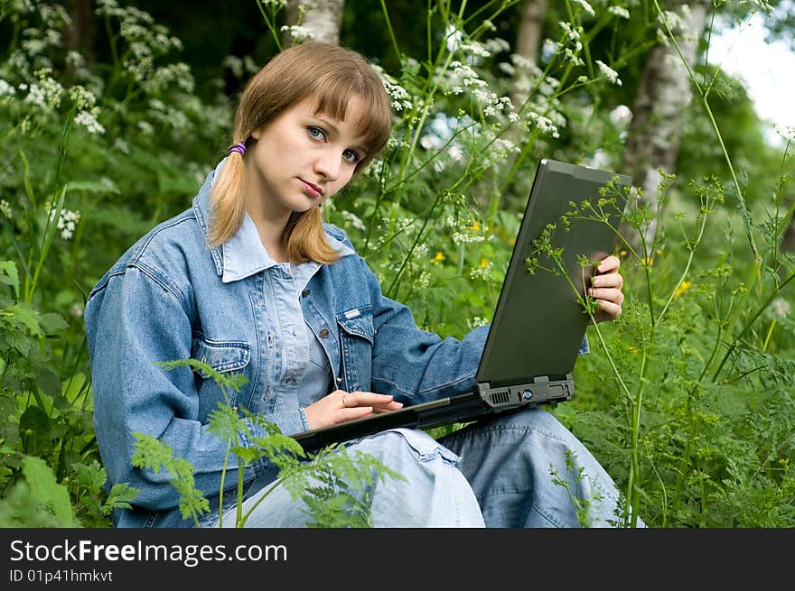 The beautiful girl with the laptop in park sits in a green grass. The beautiful girl with the laptop in park sits in a green grass