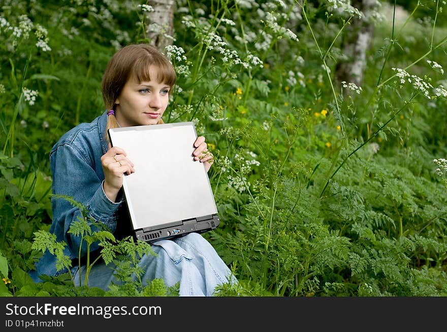 The beautiful girl with the laptop in park sits in a green grass. The beautiful girl with the laptop in park sits in a green grass