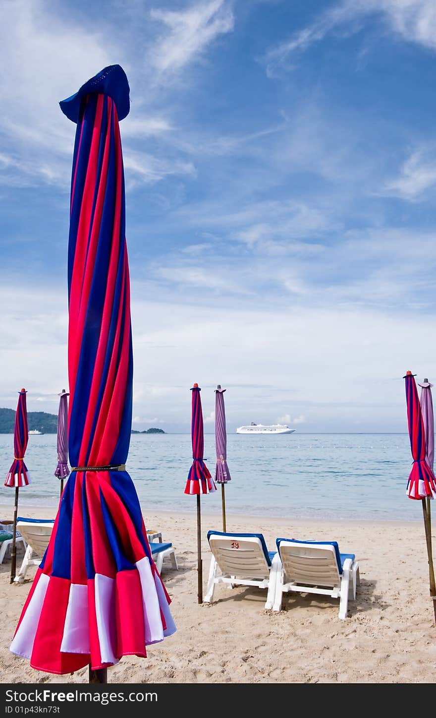 A beach is empty early in the morning, the umbrellas are tied up ready for the influx of holiday makers. the chairs are positioned facing the calm ocean and a cruise liner can be seen on the horizon. A beach is empty early in the morning, the umbrellas are tied up ready for the influx of holiday makers. the chairs are positioned facing the calm ocean and a cruise liner can be seen on the horizon.