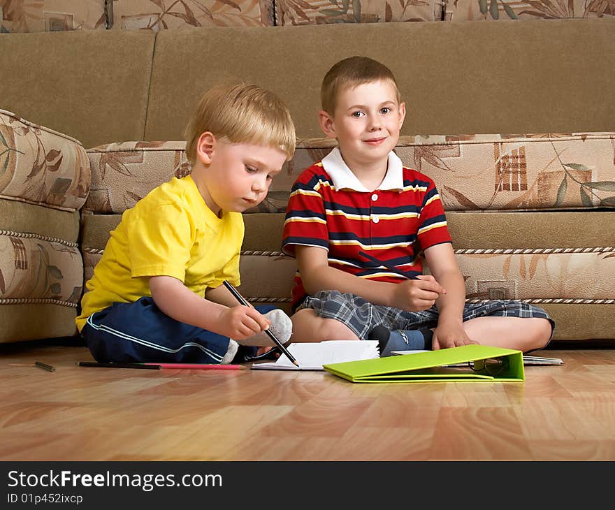 Two boys draw with paints sitting on floor