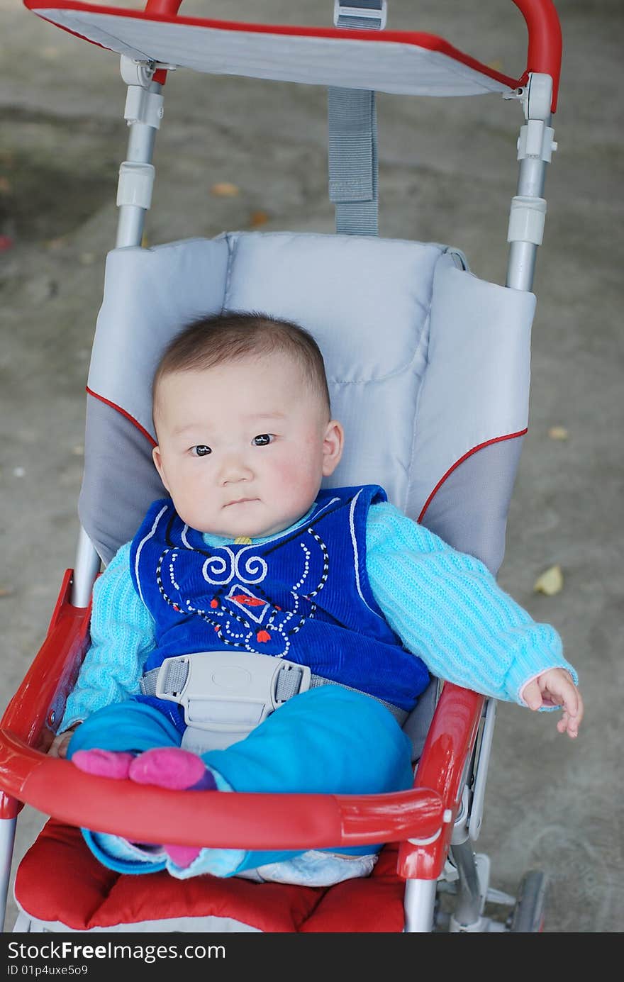 Cute baby boy sitting in red baby carriage