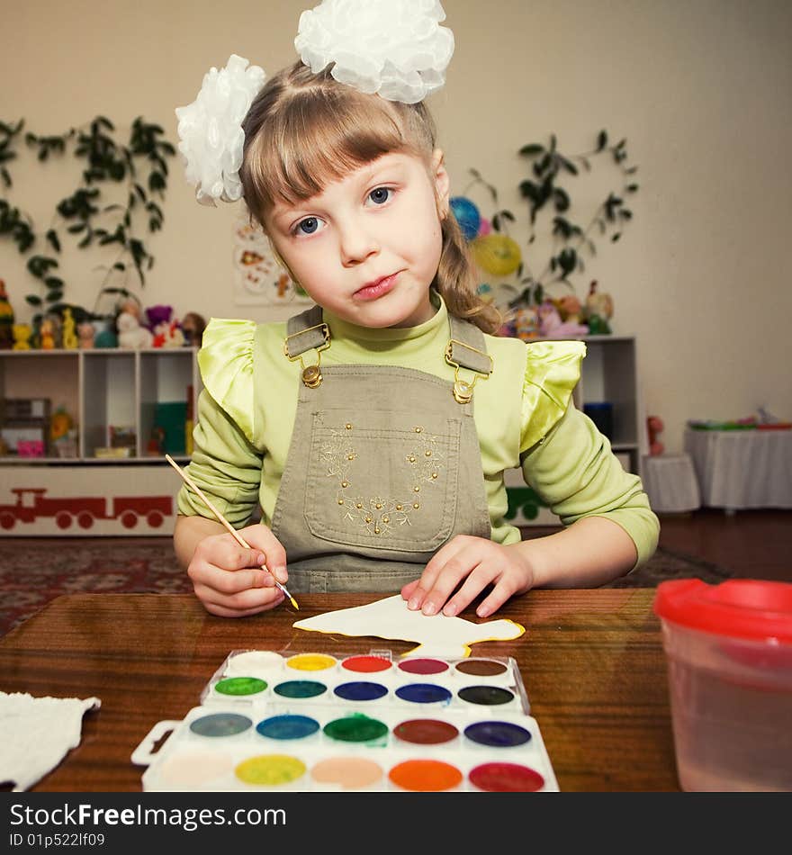 A little girl sitting at the table and painting gouache in a kindergarten. A little girl sitting at the table and painting gouache in a kindergarten