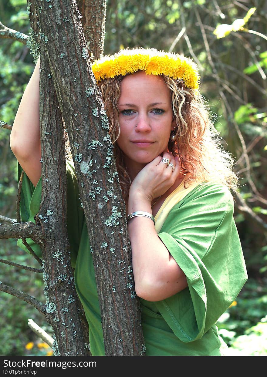 Curly girl with dandelion chain on head standing behind thin tree