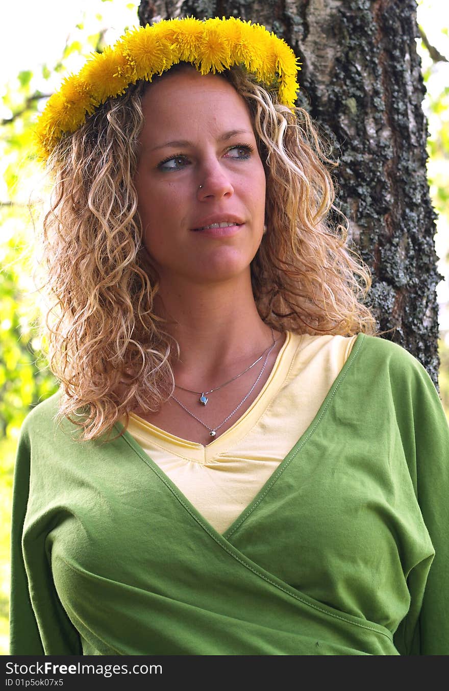 Curly girl with dandelion chain on head standing in front of birch tree