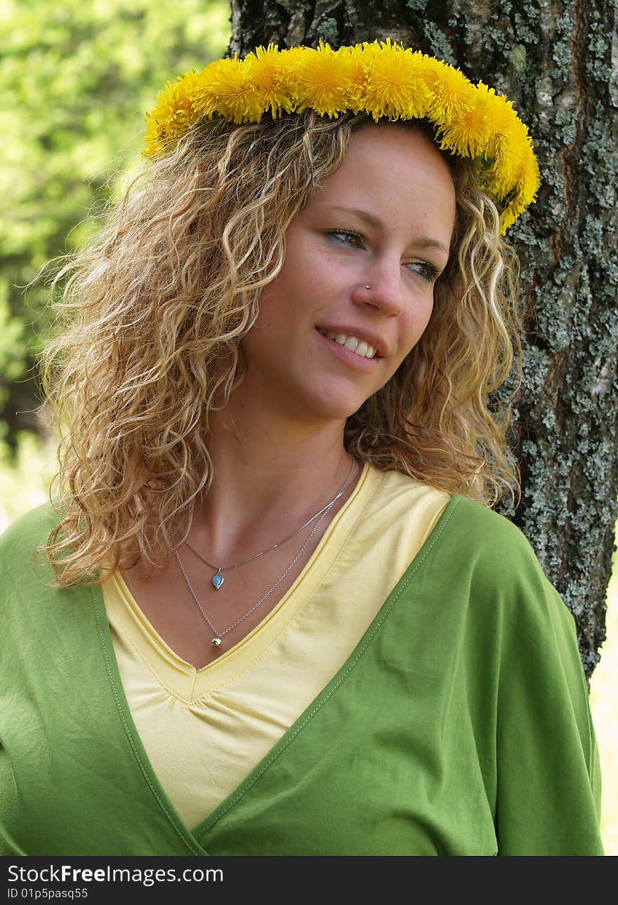 Curly girl with dandelion chain on head standing in front of birch tree