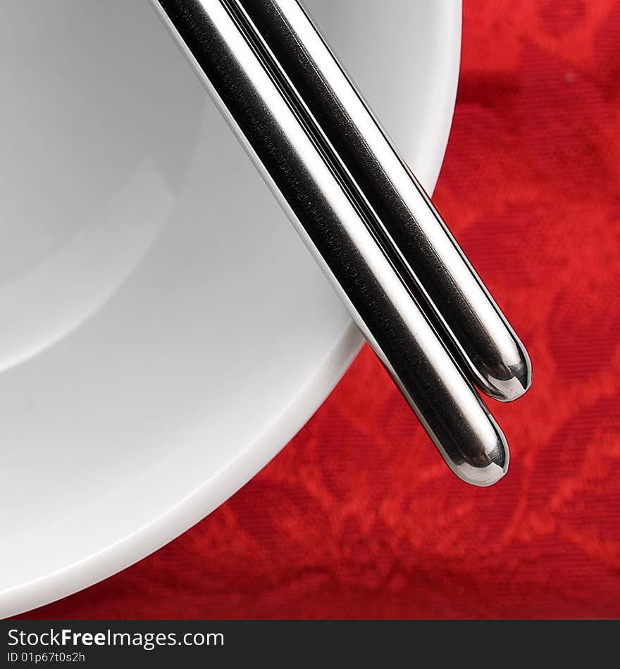 Close up shot of chopsticks on a white bowl over red table cloth