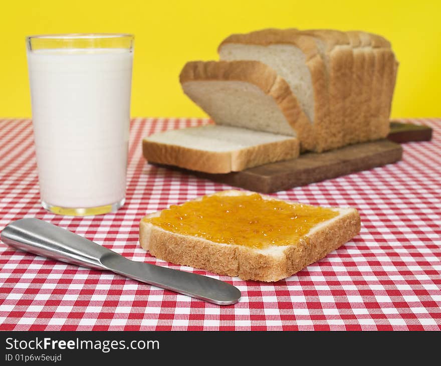 A slice of bread spread with jam beside a loaf of bread and a glass of milk. A slice of bread spread with jam beside a loaf of bread and a glass of milk.