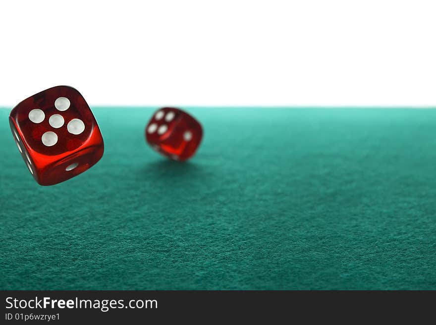 Two red dices rolling over a green felt against a white background.