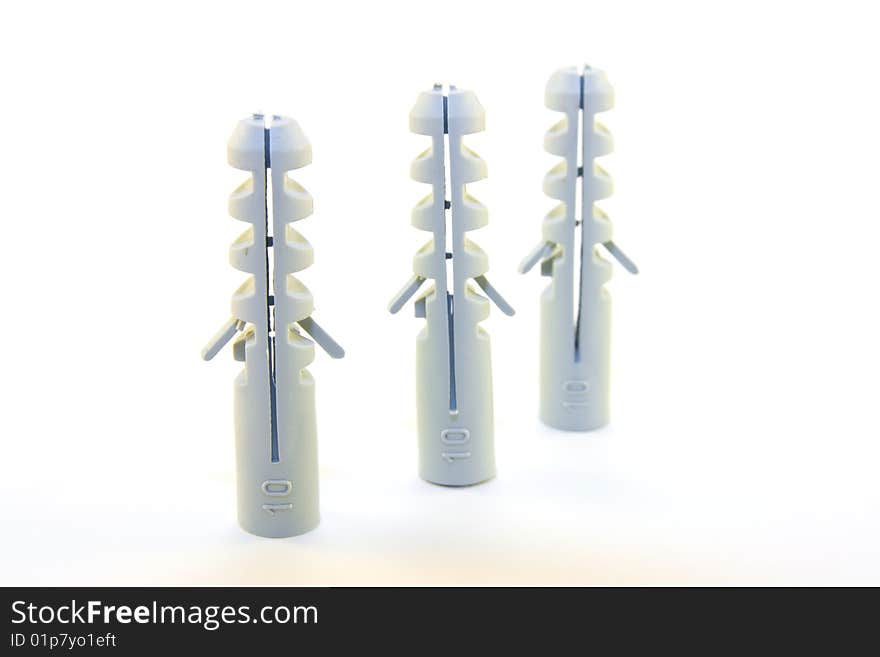 Three grey plastic wall plugs in a row on a white background. Three grey plastic wall plugs in a row on a white background