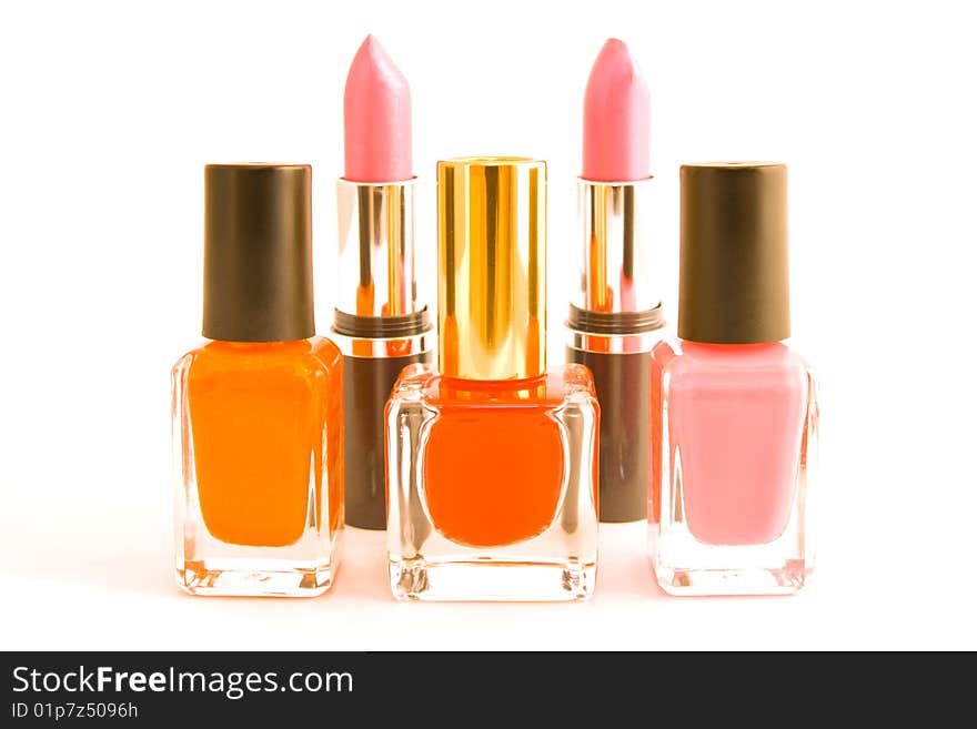 Three bottles of red, pink and orange nail polish with two pink lipsticks on a white background. Three bottles of red, pink and orange nail polish with two pink lipsticks on a white background