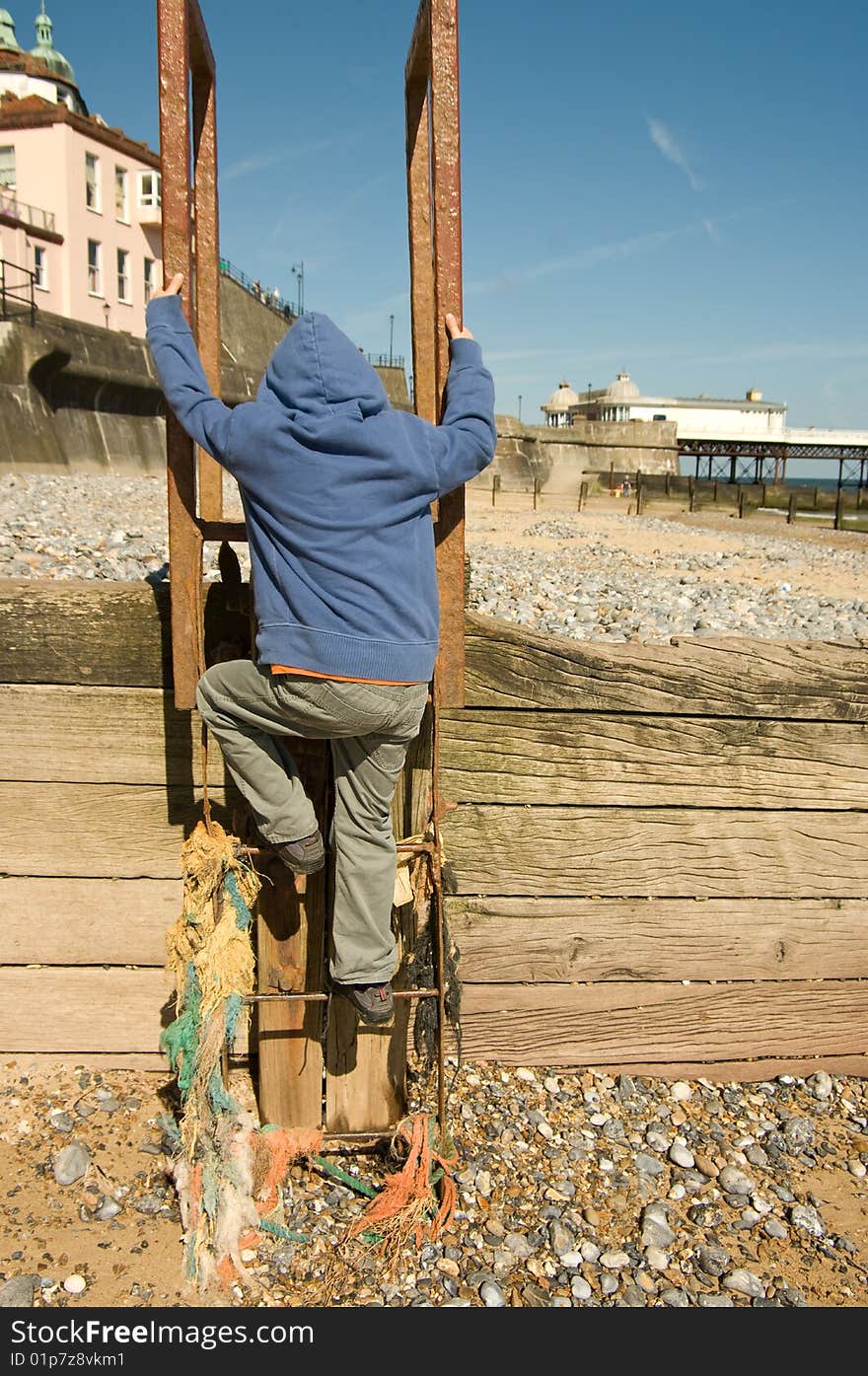 A boy climbs a ladder on Cromer beach with the pier in the background. A boy climbs a ladder on Cromer beach with the pier in the background