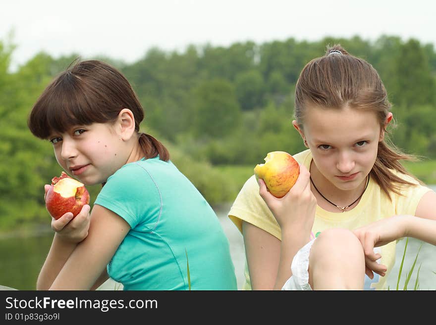 Two young girls eating apples on nature background. Two young girls eating apples on nature background