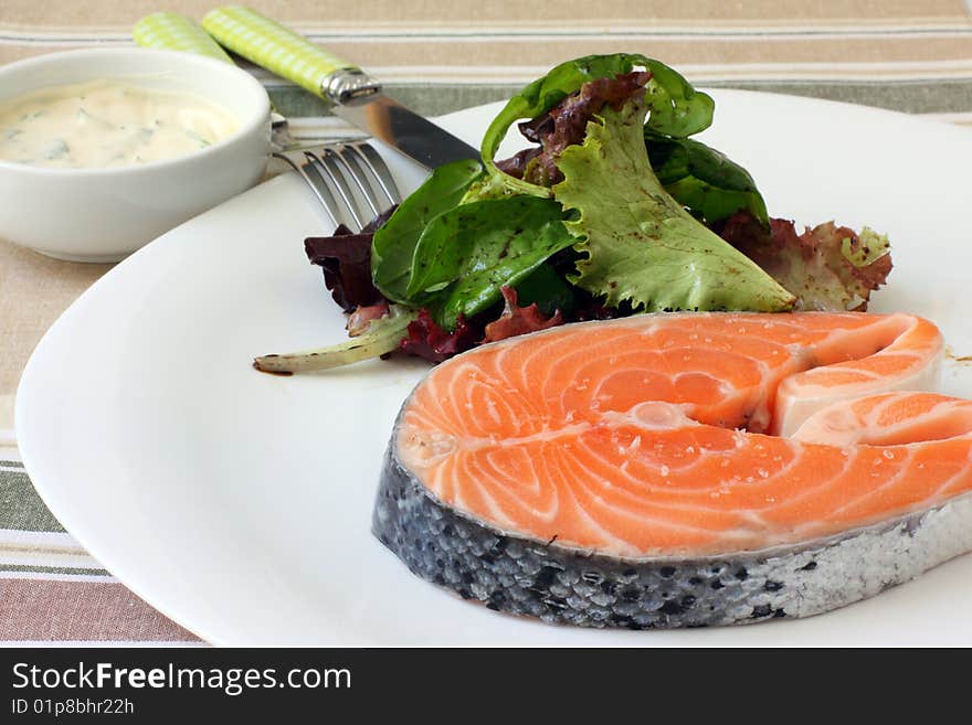 Fresh salmon steak on white platter with salad