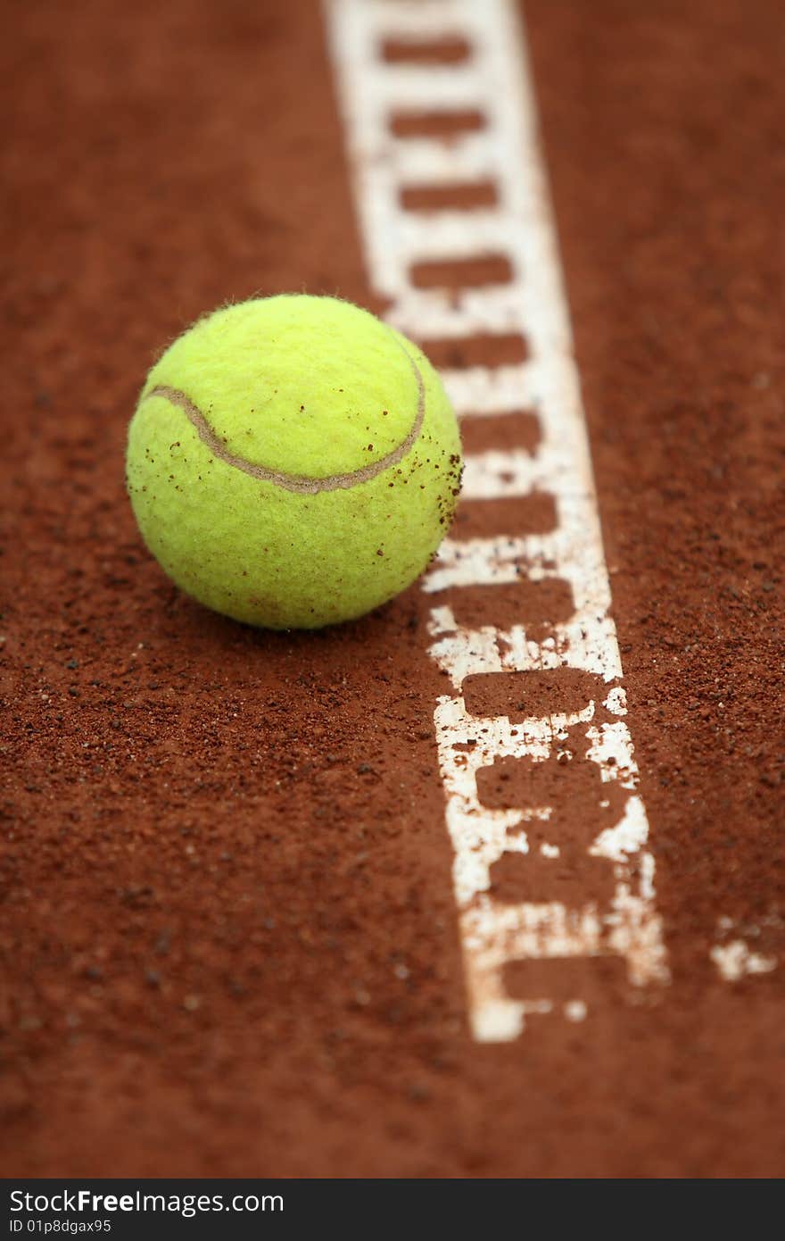 A tennis ball sits barely touching the line on a tennis court. A tennis ball sits barely touching the line on a tennis court