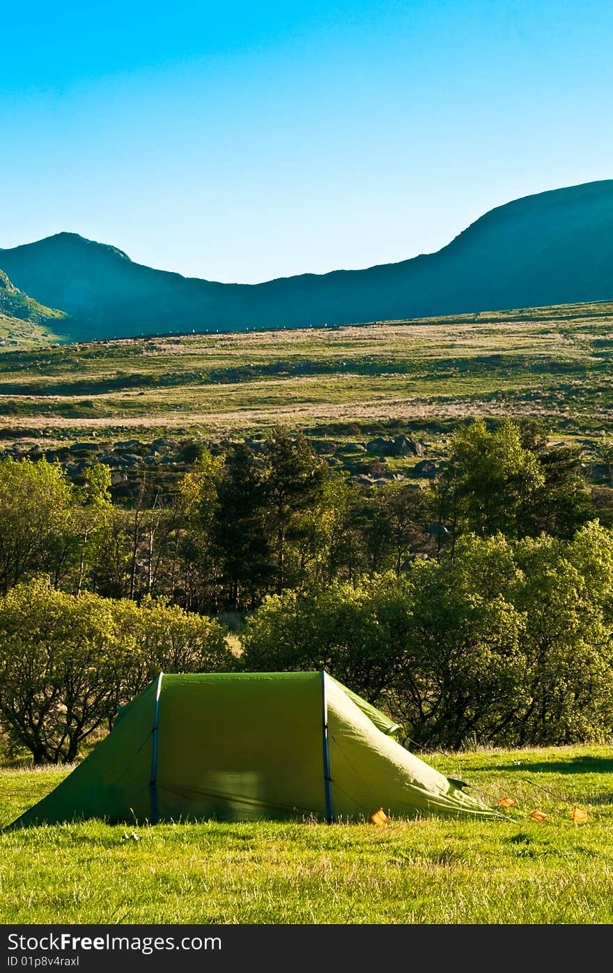 Single green tent in a field with mountains. Single green tent in a field with mountains