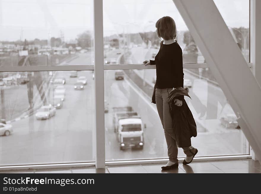 The young woman looks at highway from a shopping centre window. Black-and-white photo. The young woman looks at highway from a shopping centre window. Black-and-white photo.