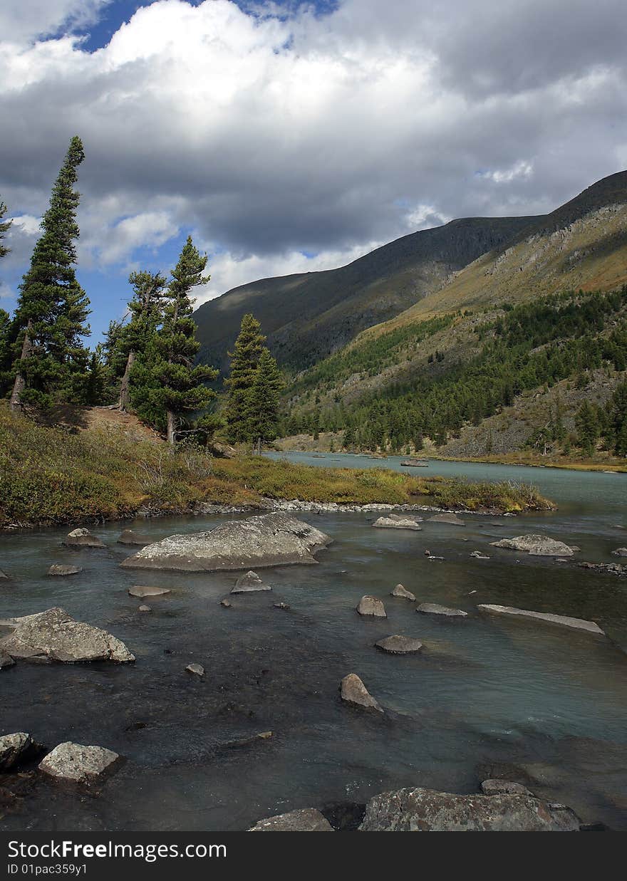 Quiet water of lake, cedar wood on coast, mountains, the sky, a cloud. The river and a train of lakes Small Kulagash, Mountain Altai, July 2008. Quiet water of lake, cedar wood on coast, mountains, the sky, a cloud. The river and a train of lakes Small Kulagash, Mountain Altai, July 2008.