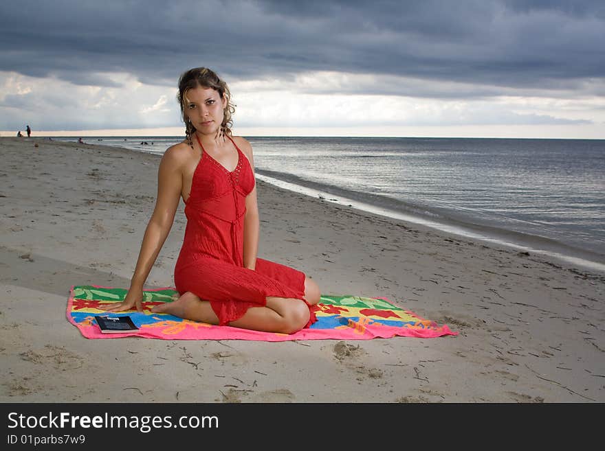 Girl with red dress on a towel, in the beach