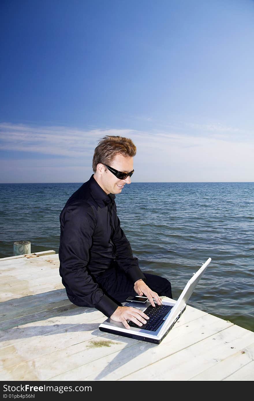 Business man using his laptop while sitting on the pier. Business man using his laptop while sitting on the pier