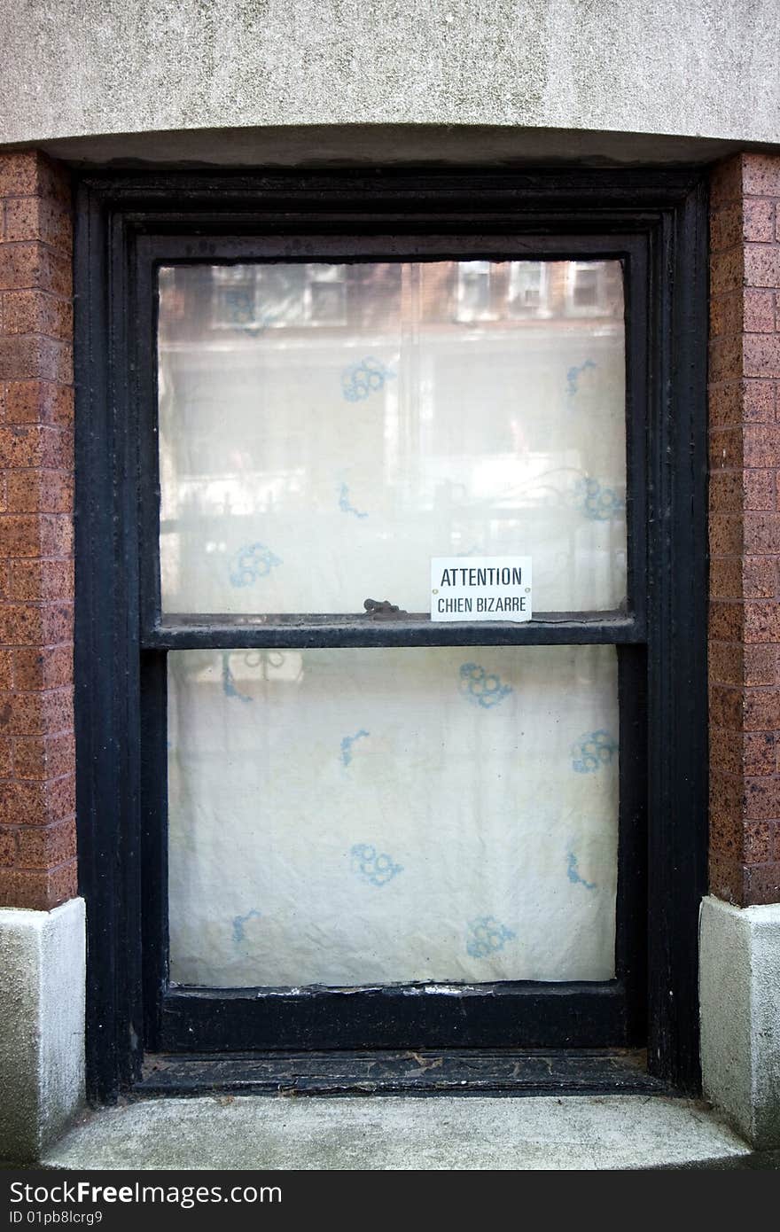 A brownstone house ground floor window with a sign in French Attention Chien Bizzarre. A brownstone house ground floor window with a sign in French Attention Chien Bizzarre