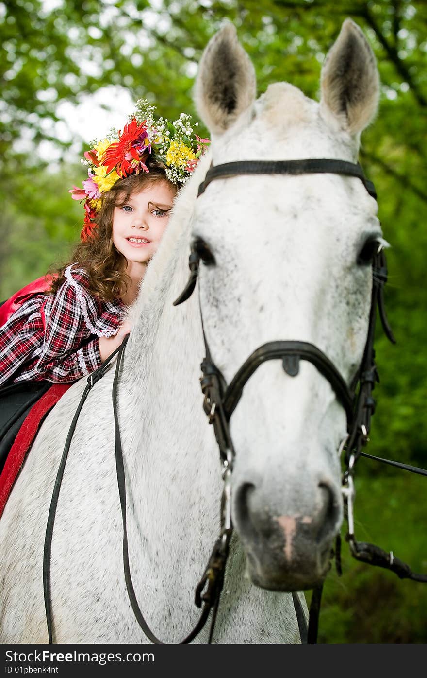 Little girl in floral wreath riding horse in the forest