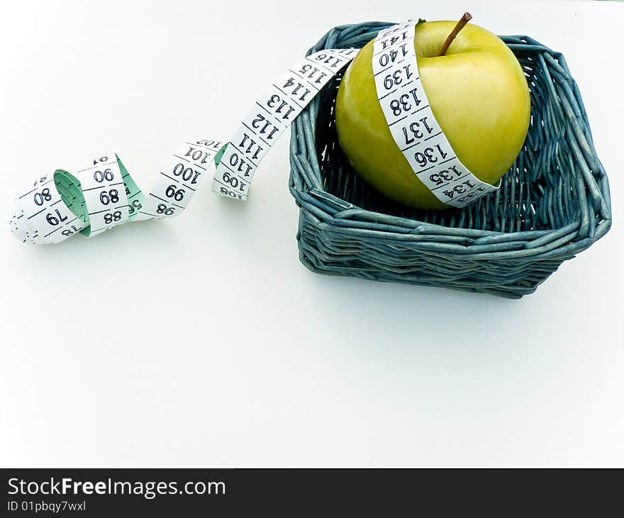 A granny smith apple in basket, surrounded by tape measure, isolated on white. Health concept. A granny smith apple in basket, surrounded by tape measure, isolated on white. Health concept.