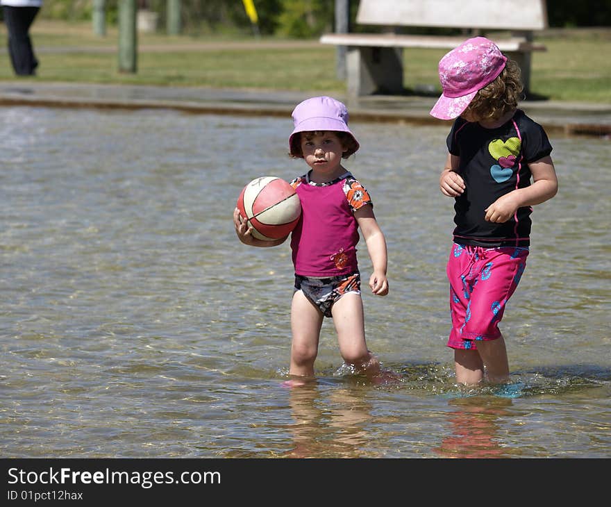 These two sisters are playing in the pond and the older sister is trying to negotiate the ball away. These two sisters are playing in the pond and the older sister is trying to negotiate the ball away.