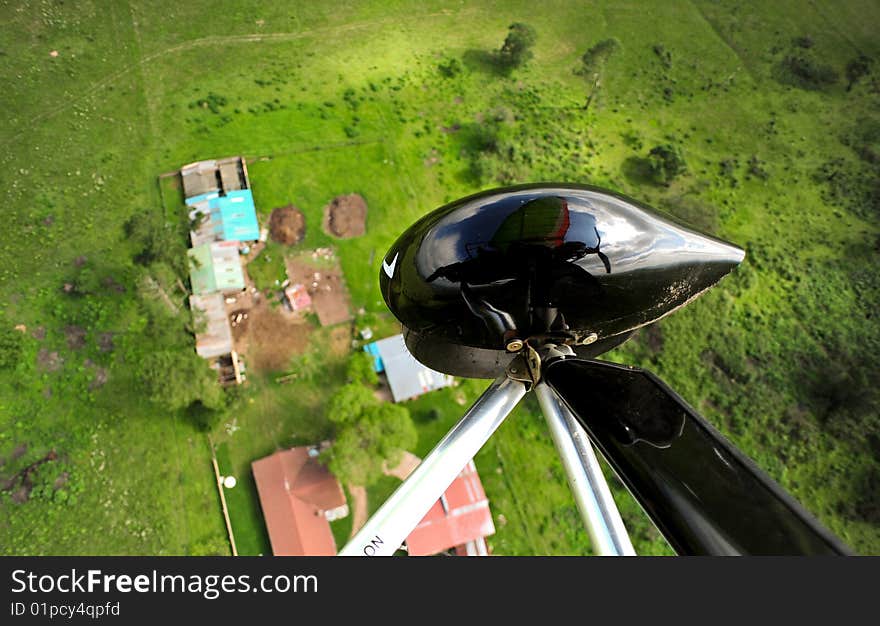 An aerial view from the seat of a microlite. you can see the wheel and the reflection of the light aircraft against the sky behind it. the lush green landscape below is dotted with small buildings. An aerial view from the seat of a microlite. you can see the wheel and the reflection of the light aircraft against the sky behind it. the lush green landscape below is dotted with small buildings.