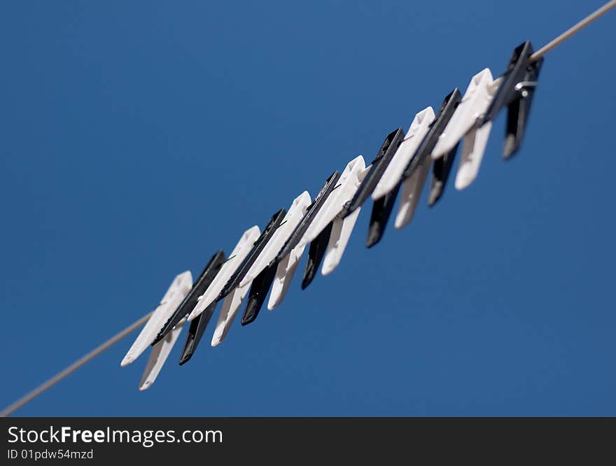 A row of black and white clothes pegs on a line with a blue sky background