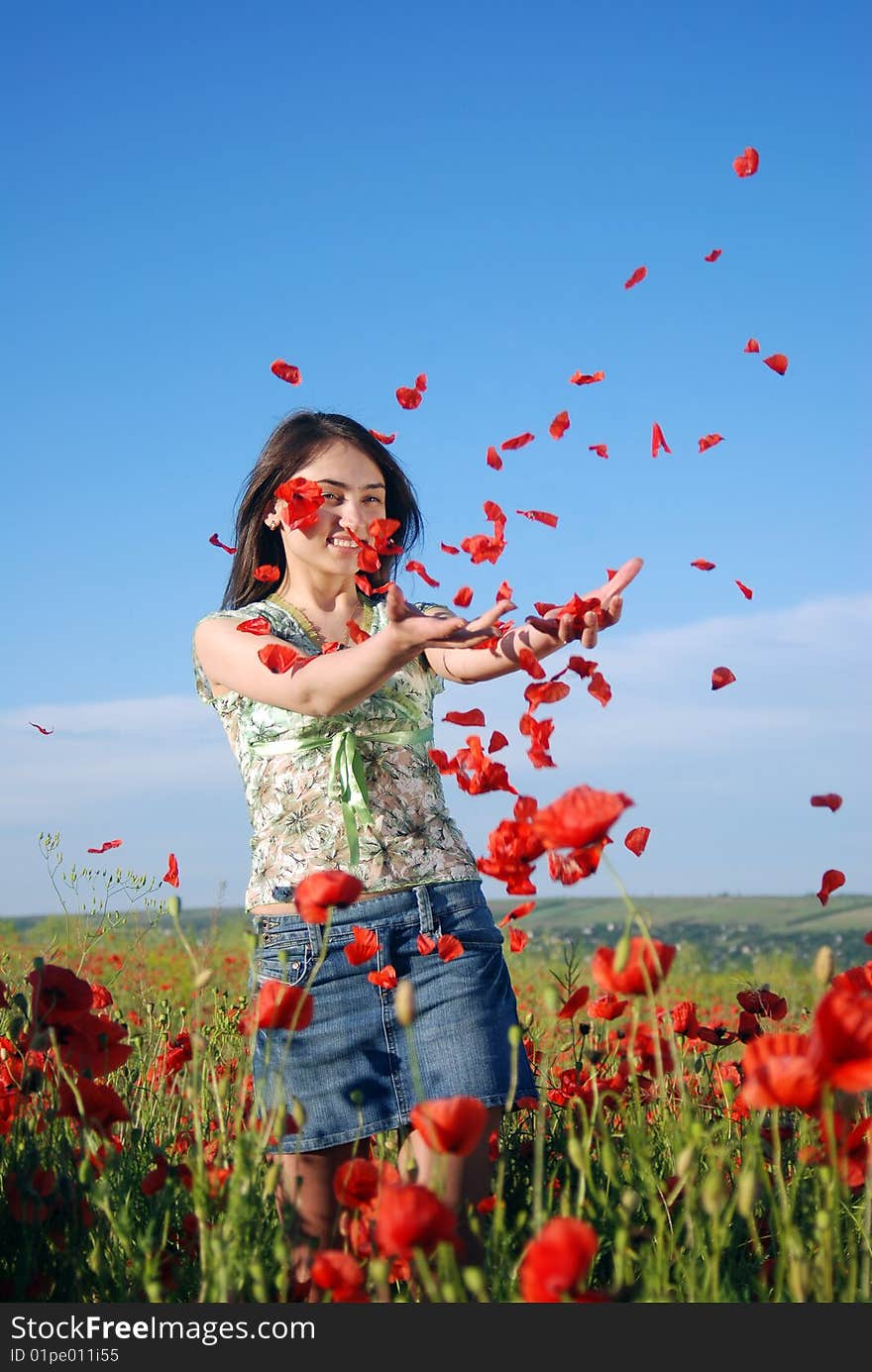 A beautiful girl standing on a field filled with red poppies and catches falling poppie petals. A beautiful girl standing on a field filled with red poppies and catches falling poppie petals